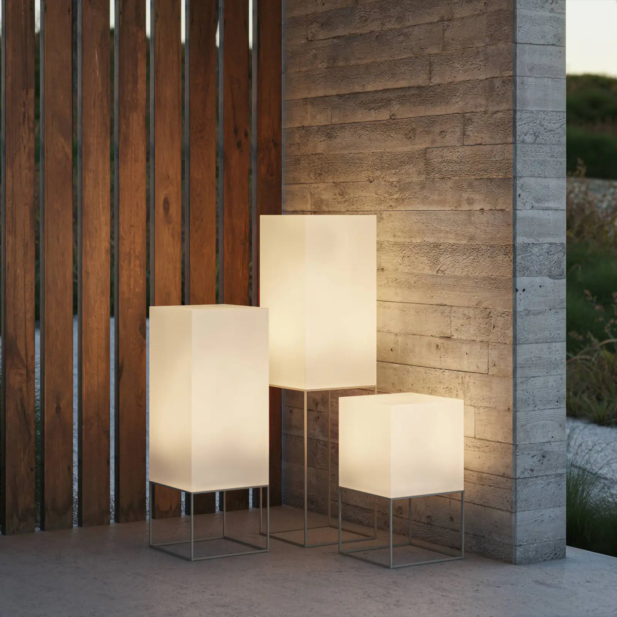 Lampadaires Vela Vondom allumés au crépuscule sur une terrasse en bois et béton