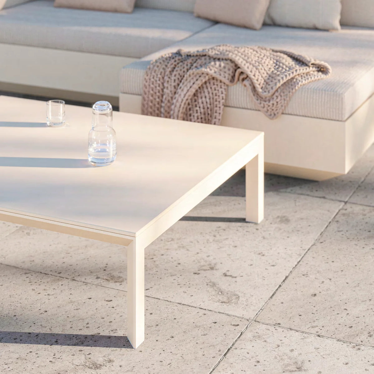 Table basse Frame crème devant un canapé modulable, carafe et verre posés dessus