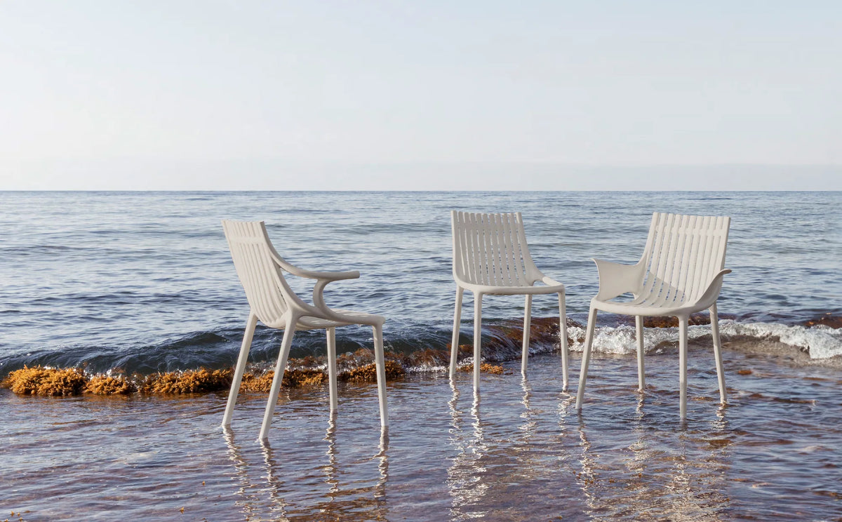 Trois chaises Ibiza Vondom écrues, avec et sans accoudoirs, les pieds dans l'eau au bord de la mer