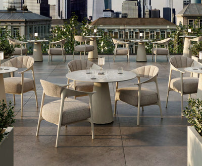 Tables rondes Gatsby taupe, hautes et basses, avec fauteuils Africa sur une terrasse d'hôtel en ville