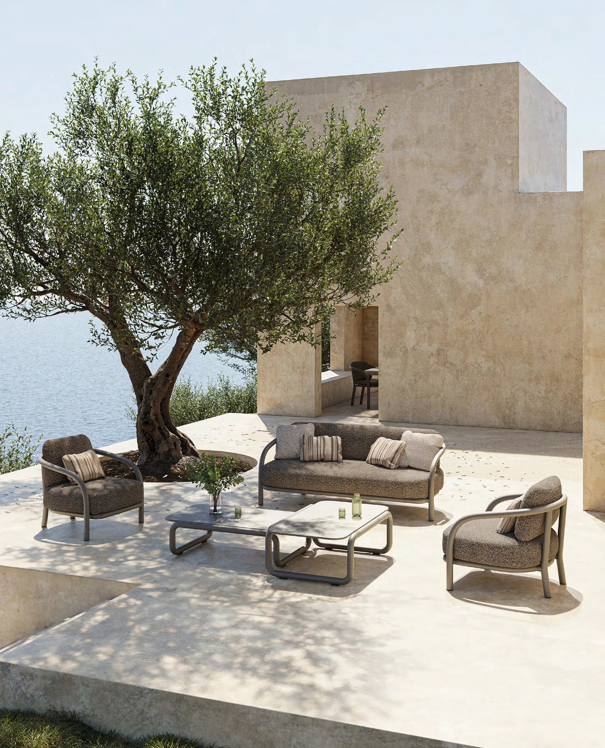 Fauteuil, canapé et tables basses Gum taupe foncé sur une terrasse en pierre avec olivier