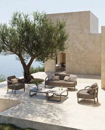 Fauteuil, canapé et tables basses Gum taupe foncé sur une terrasse en pierre avec olivier