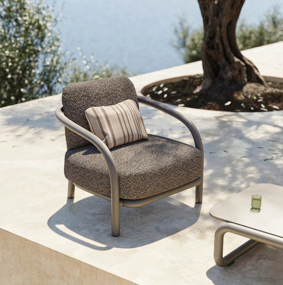 Fauteuil Gum taupe foncé et coussin rayé près d'un olivier, table basse au premier plan