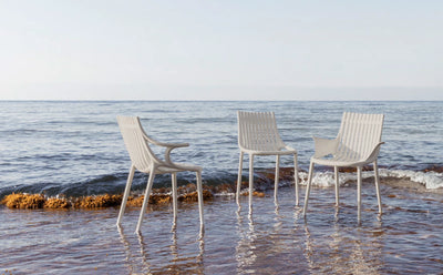 Trois chaises Ibiza Vondom écrues, avec et sans accoudoirs, les pieds dans l'eau au bord de la mer