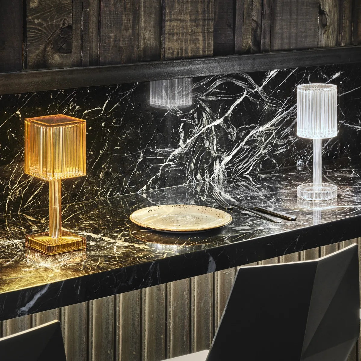 Lampade da tavolo Gatsby Vondom accese su un bancone in marmo nero, quadrata con piede ambra e rotonda cristallo
